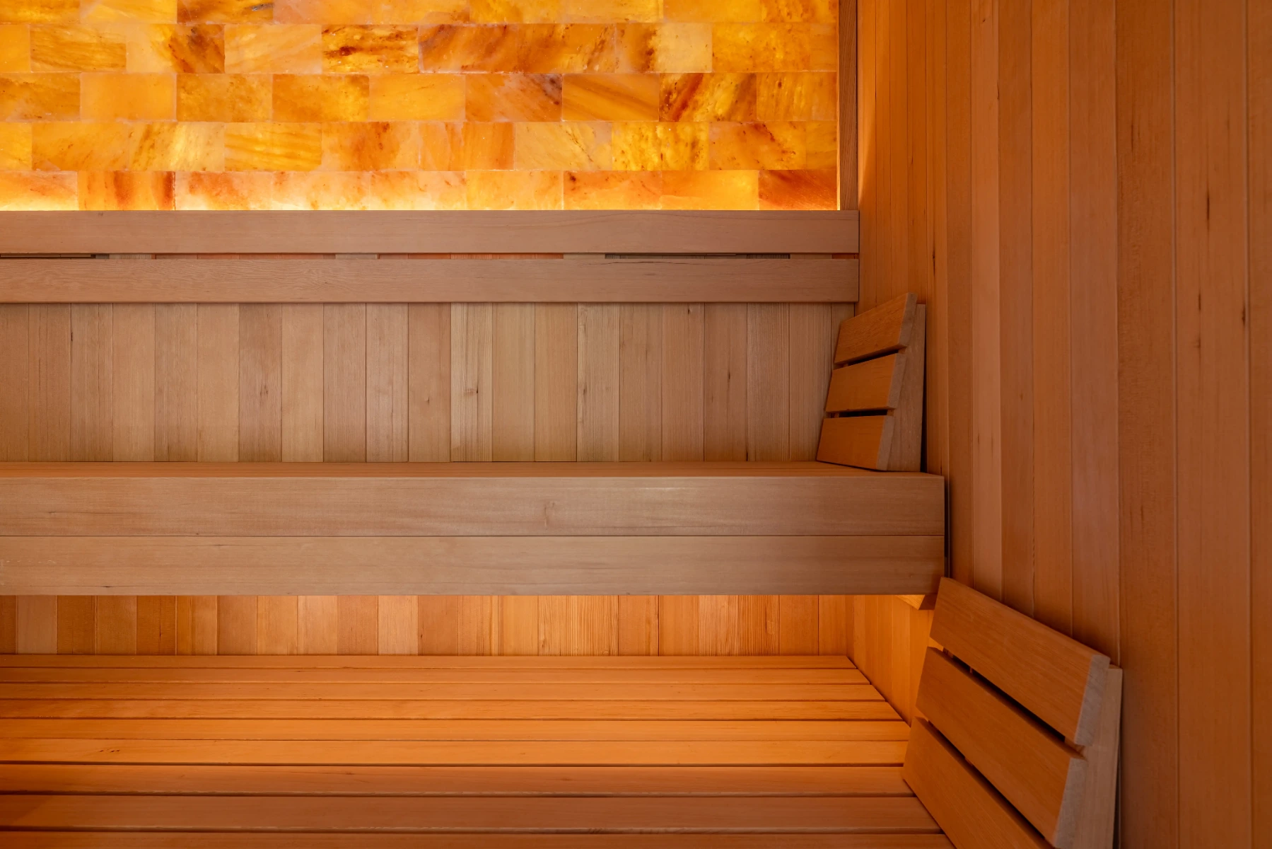 Interior of a custom cedar sauna with two-tier benches and a glowing Himalayan salt wall, creating a warm and inviting wellness environment.